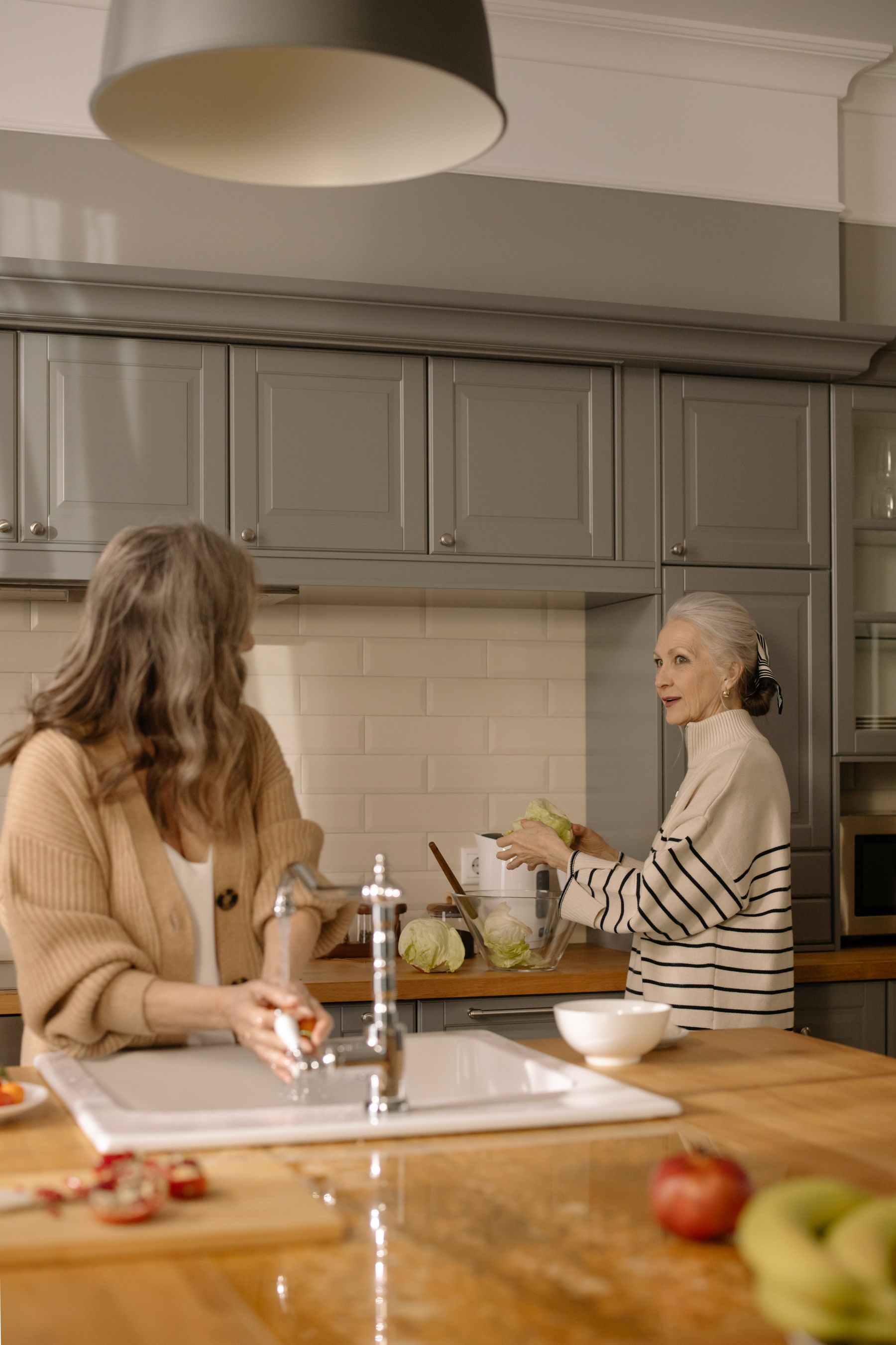 Two women enjoying conversation while preparing food together at home